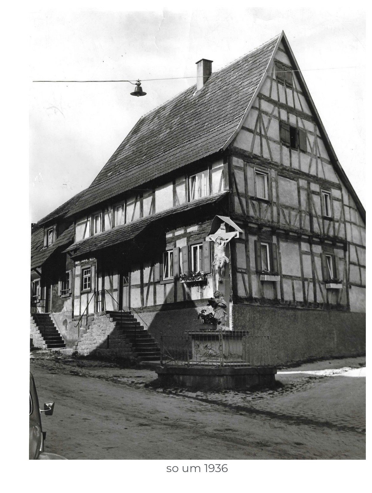 Historische Schwarzweißaufnahme: zweistöckiges Fachwerkhaus an einer Straßenecke in Neibsheim, davor ein Wegkreuz mit Kruzifix